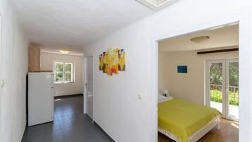A room with a bed, a small kitchenette, a window, and a door leading to a balcony.