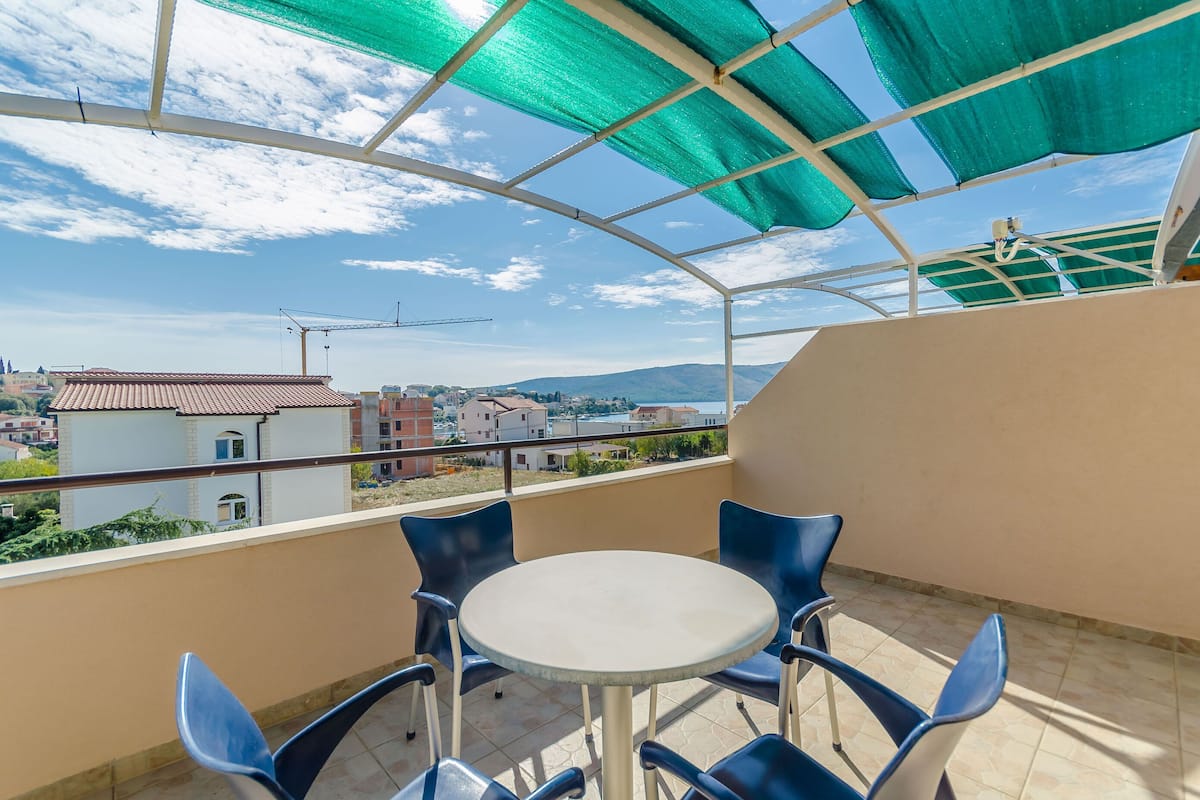 Un balcon avec une table et des chaises, une vue sur les bâtiments et les montagnes, et une végétation luxuriante.
