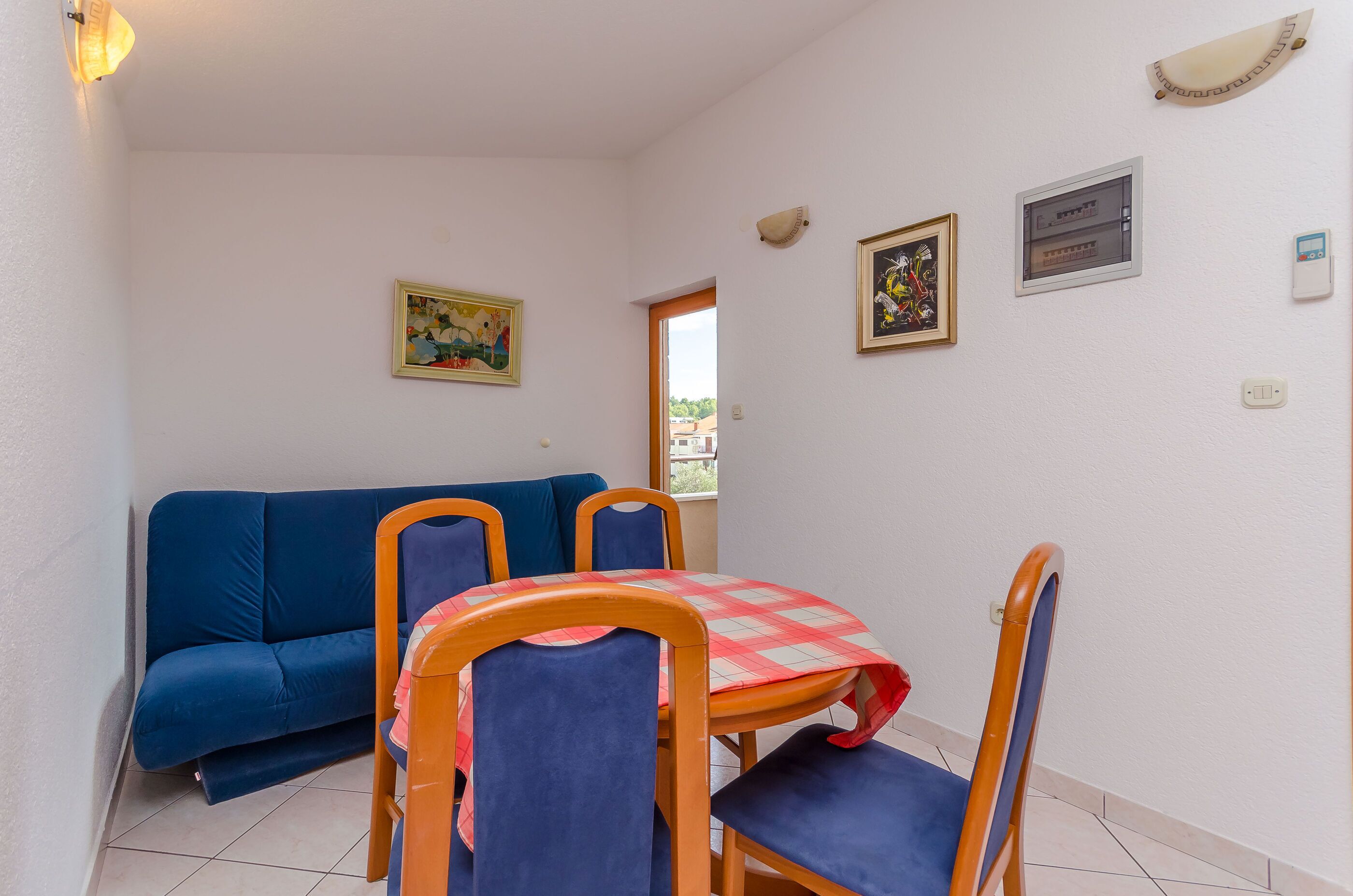 Ein kleiner Raum mit einem blauen Sofa, einem Tisch mit Stühlen und zwei gerahmten Kunstwerken an der Wand.