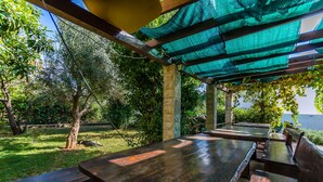 Un espace extérieur aménagé en terrasse, avec des tables et des bancs en bois, entouré de verdure et d’arbres.