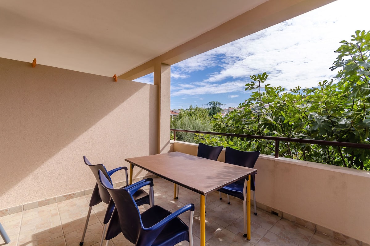 Un balcon avec une table et des chaises, une balustrade et une vue sur la verdure et les bâtiments.