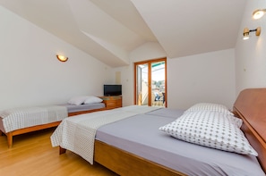 A bedroom with two single beds, a wooden dresser, a television, and a sliding glass door leading to an outdoor area. - Apartments Milivoj (Seget)