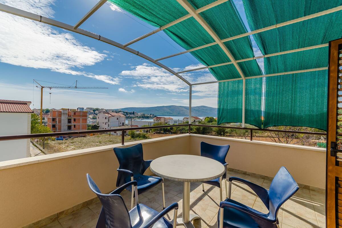 Un balcon avec une table et des chaises, une vue sur les bâtiments et les montagnes, et une végétation luxuriante.