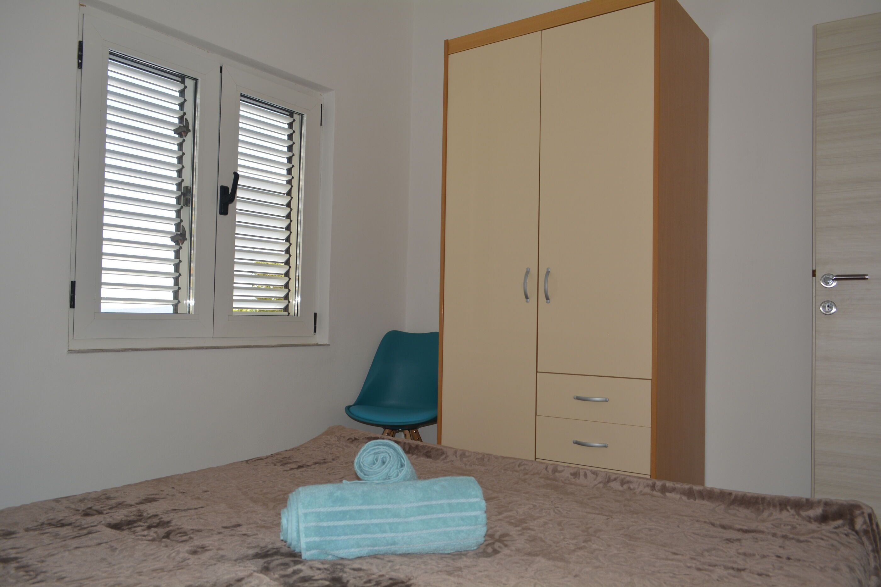 Un dormitorio con cama, armario, silla y ventana con persianas.