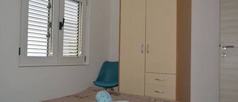 Un dormitorio con cama, armario, silla y ventana con persianas.