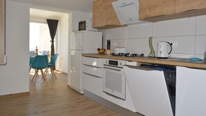 Et moderne køkken med hvide hårde hvidevarer, en træbordplade og et spiseområde med turkise stole.