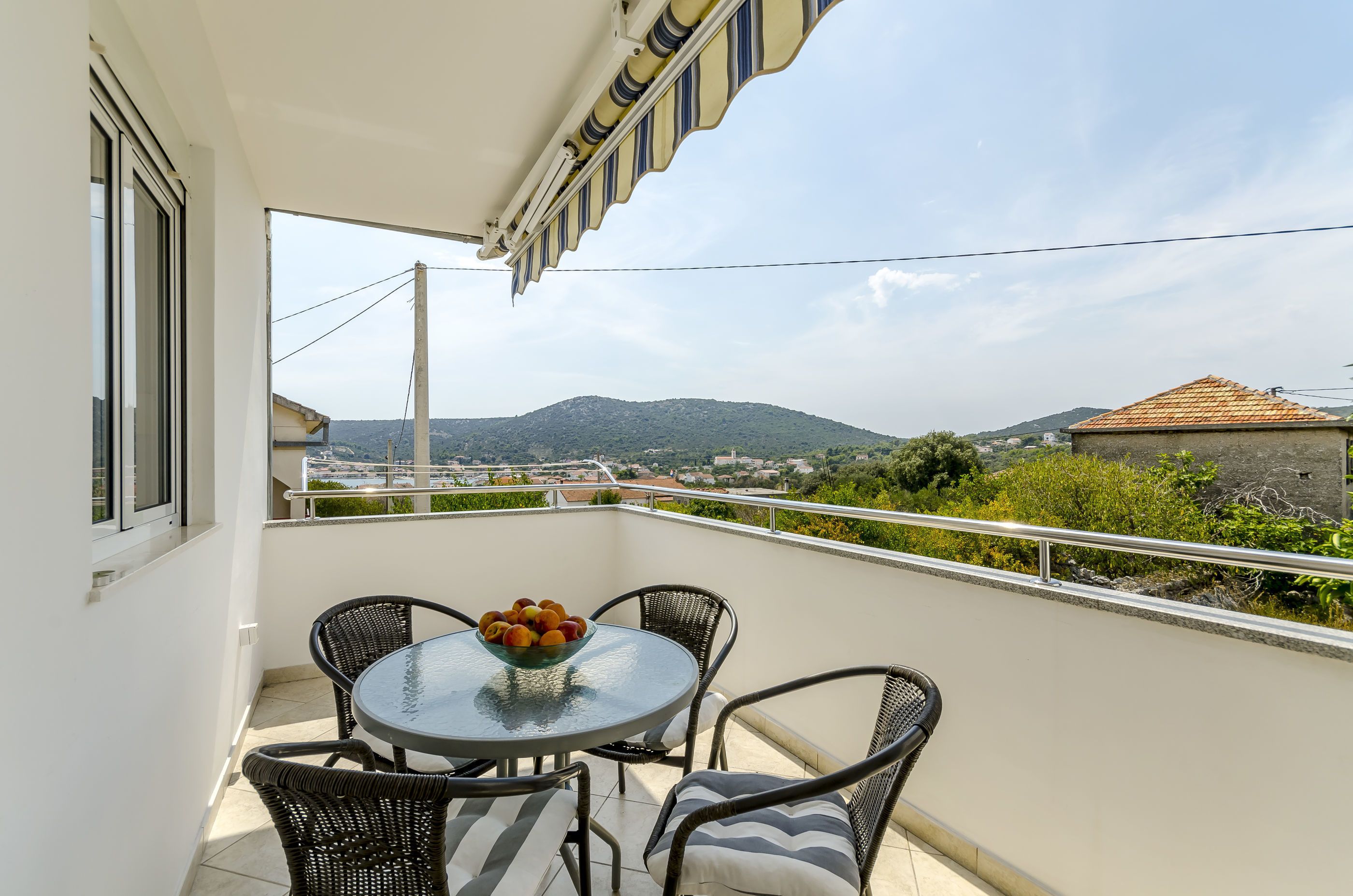Een balkon met een tafel en stoelen, een fruitschaal en uitzicht op een berg en stad.