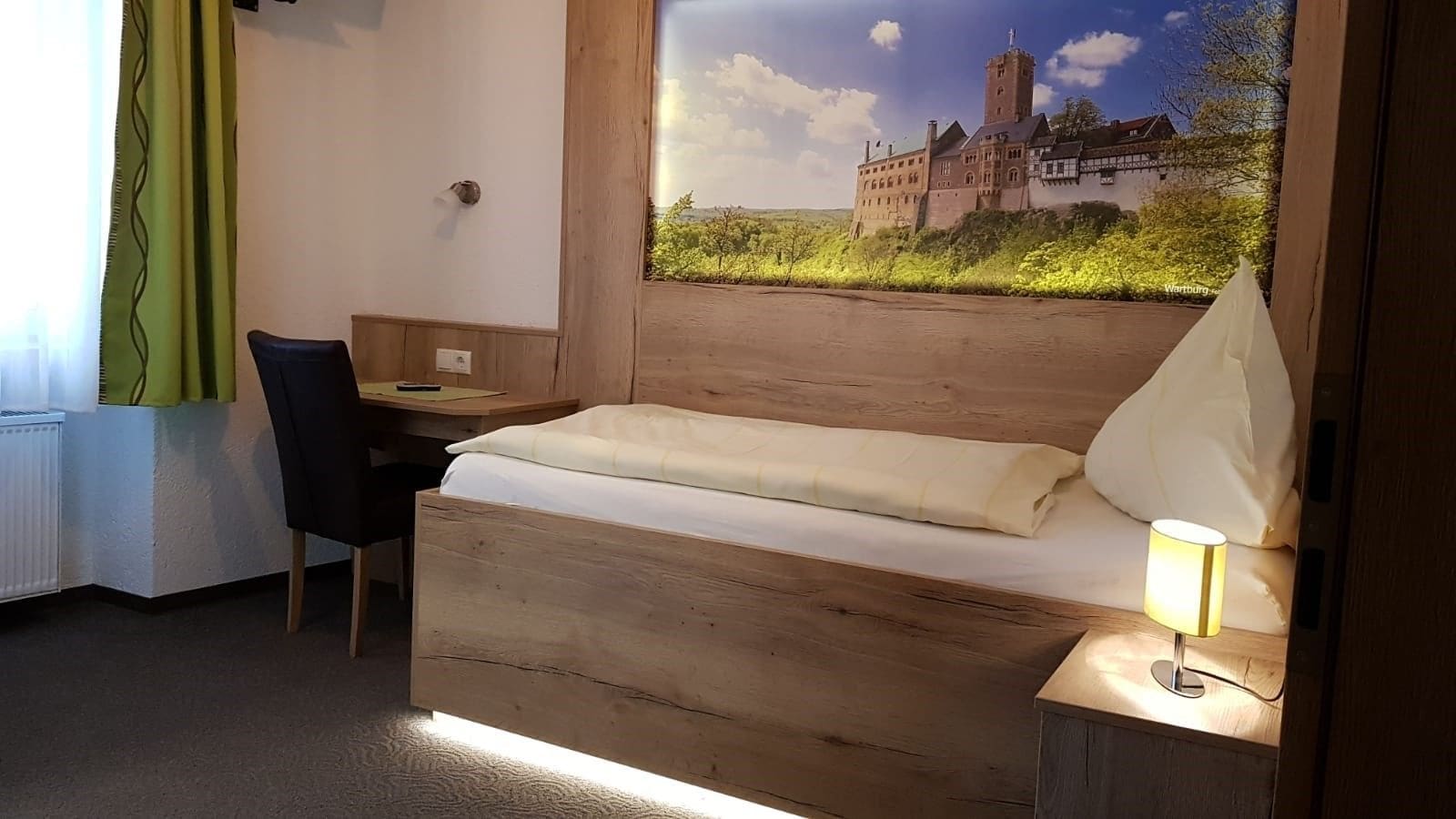 Habitación de hotel con cama de madera, un escritorio y una silla. Se ve un castillo por la ventana.