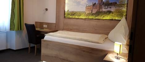A hotel room with a wooden bed, a desk, and a chair. There is a window with a view of a castle.