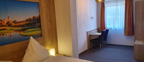 Una habitación de hotel con una cama, un escritorio con sillas, un cuadro en la pared y una ventana con cortinas.