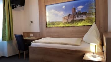 Habitación de hotel con cama de madera, un escritorio, una silla, televisor montado en la pared y un ventanal con vistas a un castillo.