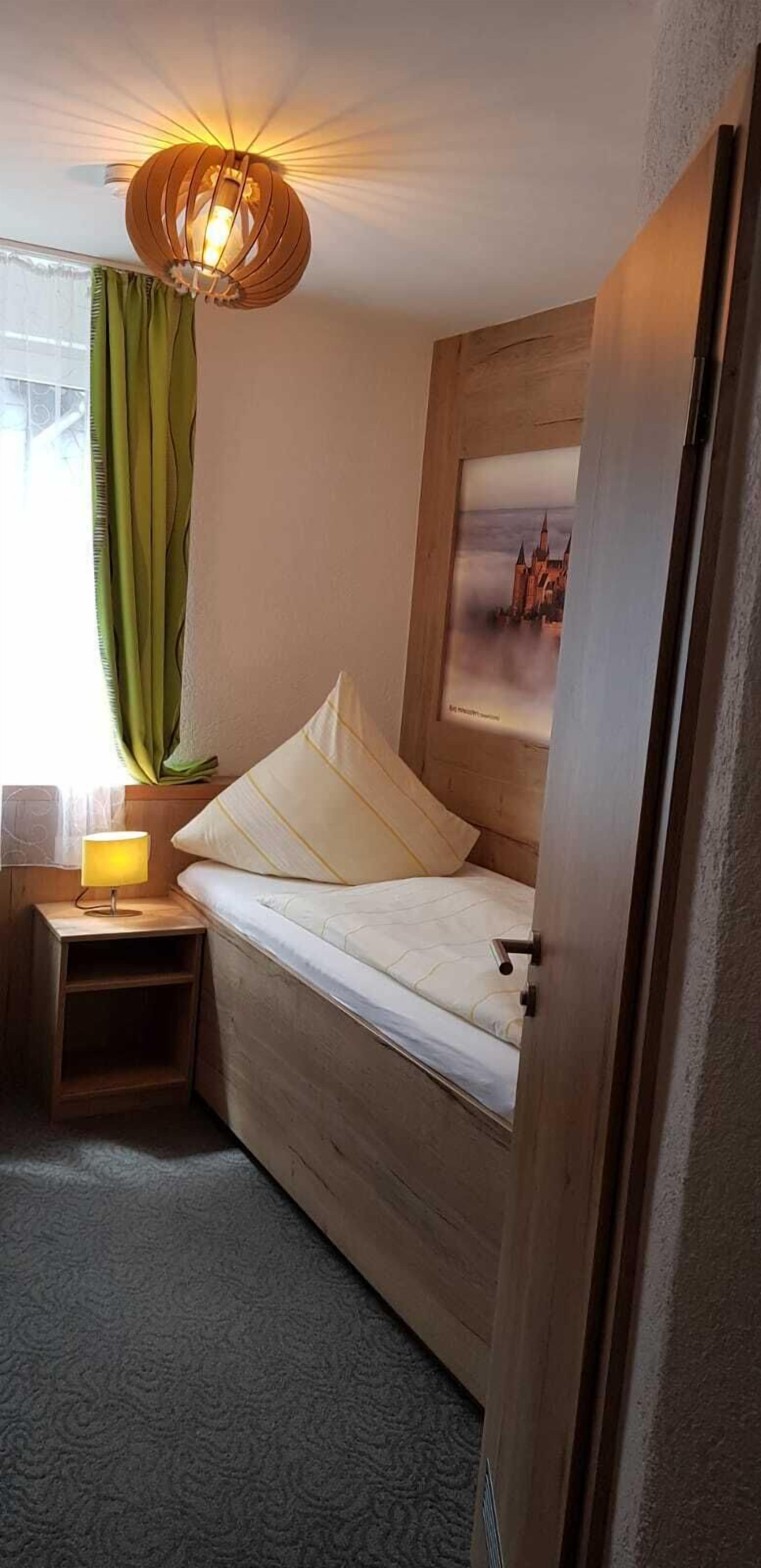 Een knus interieur met een bed, een bedlampje, een ingelijst kunstwerk aan de muur en een raam met gordijnen.