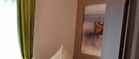 Un cuarto acogedor con cama, lámpara de noche, un cuadro enmarcado en la pared y una ventana con cortinas.
