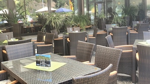 Un espace extérieur aménagé avec des meubles en osier et des tables en verre, entouré de plantes en pot et de parasols.