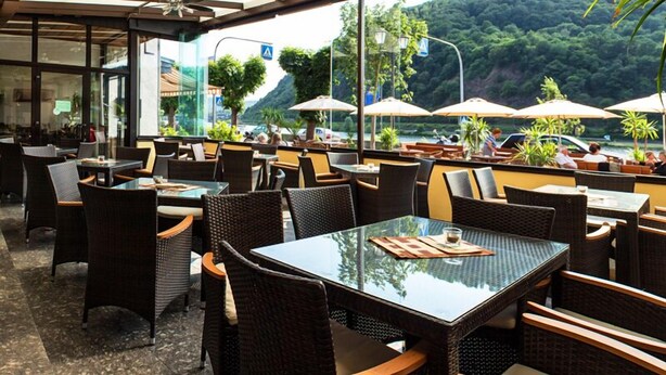 Un restaurant en plein air avec des meubles en osier, des tables en verre et des parasols.