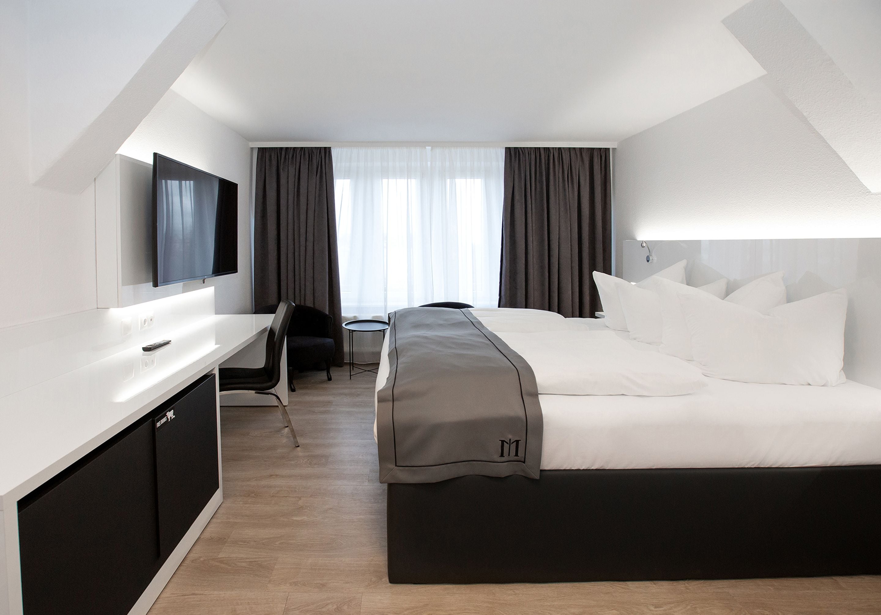 Una habitación de hotel moderna con cama, escritorio, silla y televisor.