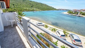Un balcón con vistas a la costa, que incluye una carretera con coches aparcados y un barco en el agua.