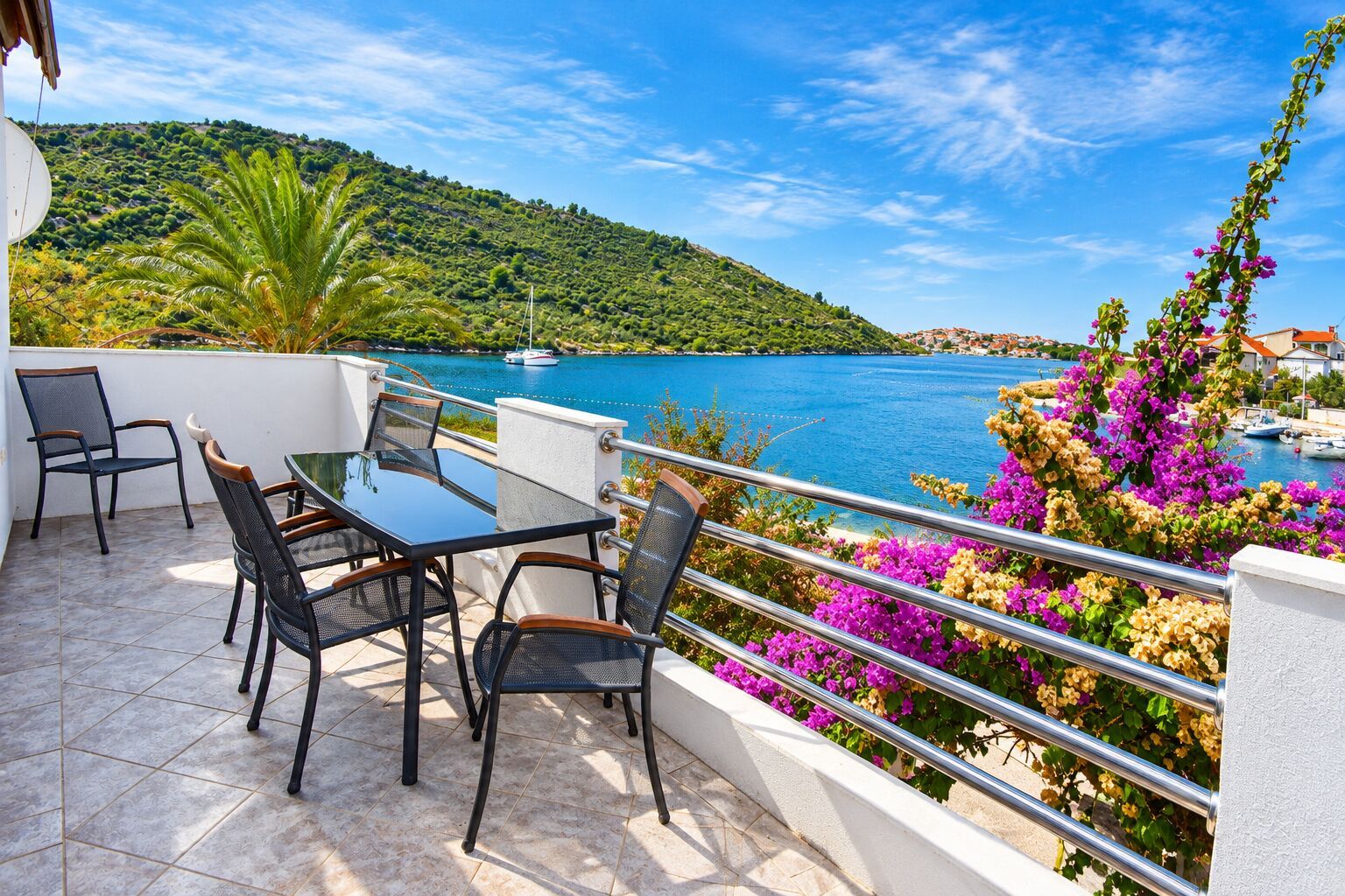 Eine Terrasse mit Tisch und Stühlen, mit Blick auf ein Gewässer und eine hügelige Landschaft.