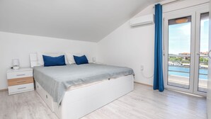Un dormitorio con cama, mesita de noche, lámpara y vista a un cuerpo de agua a través de una ventana.
