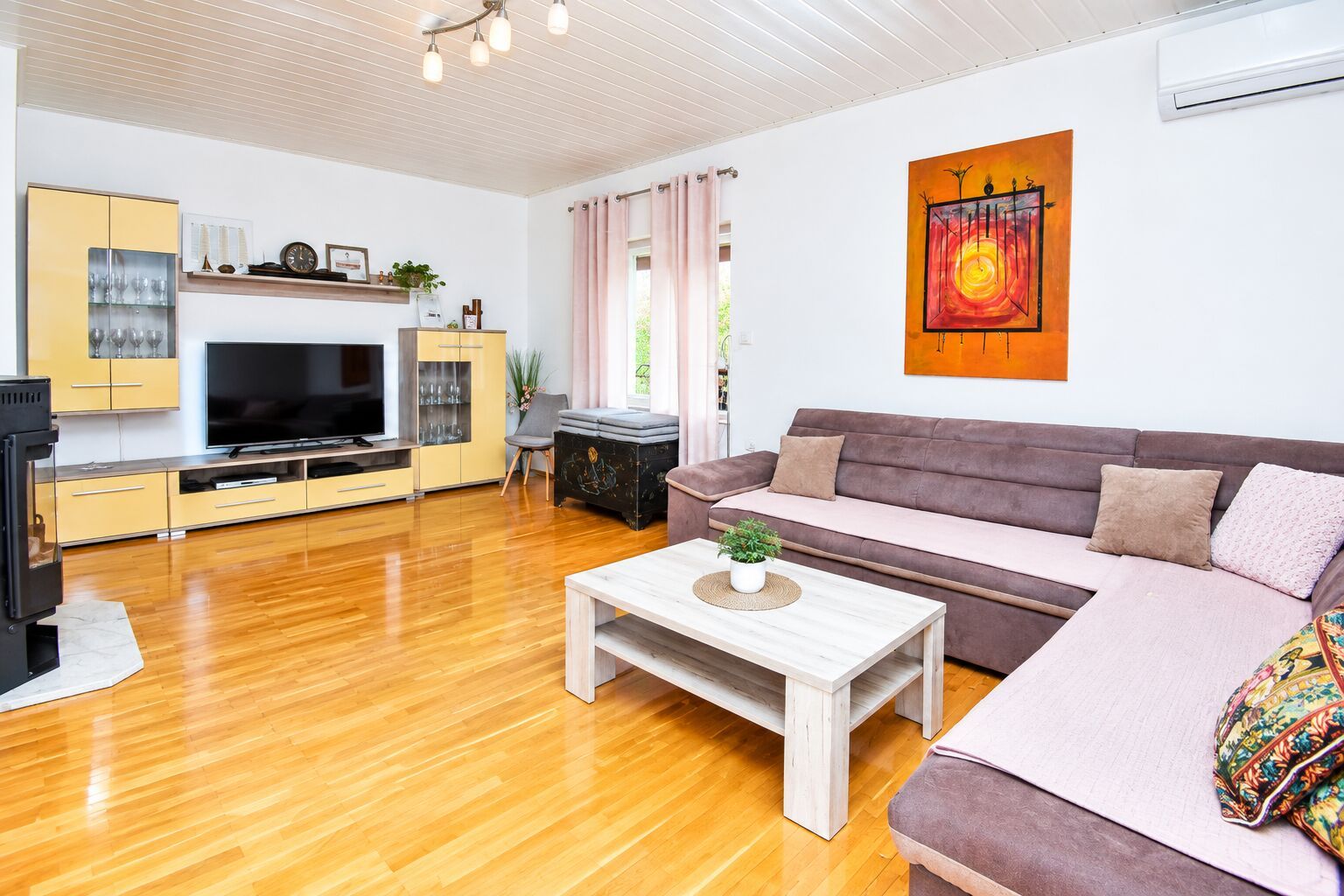 A modern living room with a flat-screen TV, wooden flooring, a sofa, and a coffee table with a plant.