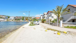 Zona residencial costera con una playa arenosa, coches estacionados y una grúa de construcción al fondo.