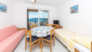 A room with a sofa, a table with chairs, a bed, a ceiling fan, a TV, and a view of the sea. - Apartments Val (Vinisce)