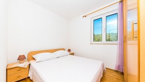 A bedroom with a wooden bed, a nightstand, a lamp, and a window with a view of greenery. - Apartments Val (Vinisce)
