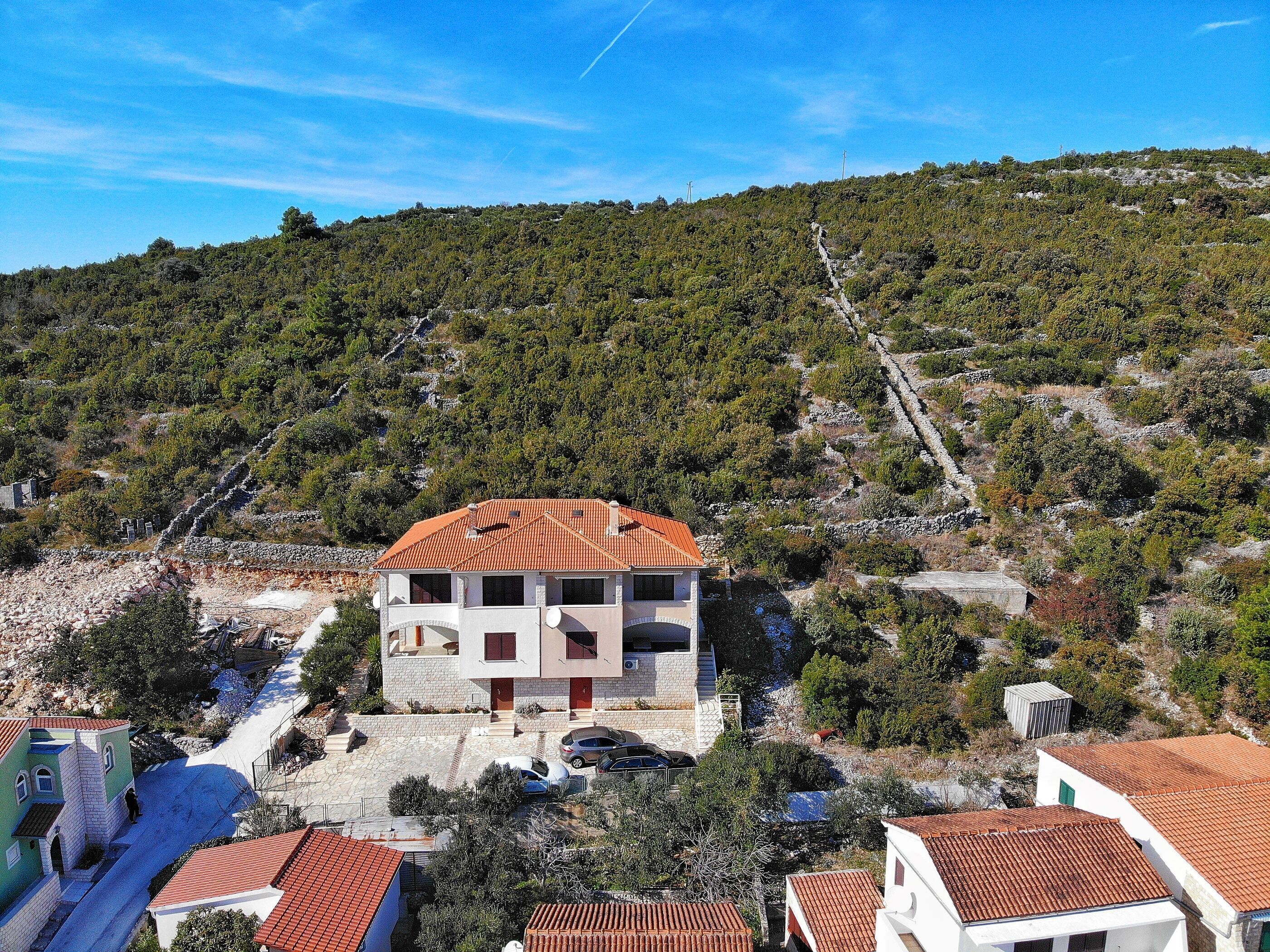 A two-story building with a red-tiled roof, situated on a hillside with a rocky terrain and sparse vegetation.
