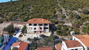 A two-story building with a red-tiled roof, situated on a hillside with a rocky terrain and sparse vegetation. - Apartments Val (Vinisce)