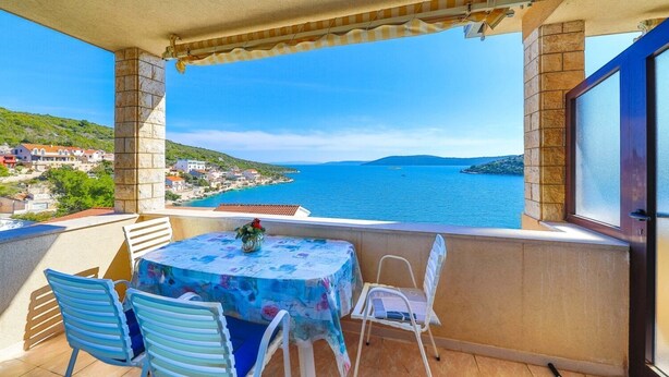 A balcony with a table and chairs, overlooking a coastal town and sea. - Apartments Val (Vinisce)