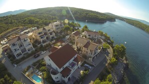 An aerial view of a coastal residential area with multiple two-story buildings, a swimming pool, and a marina with boats. - Apartment Nikola (Jelsa)