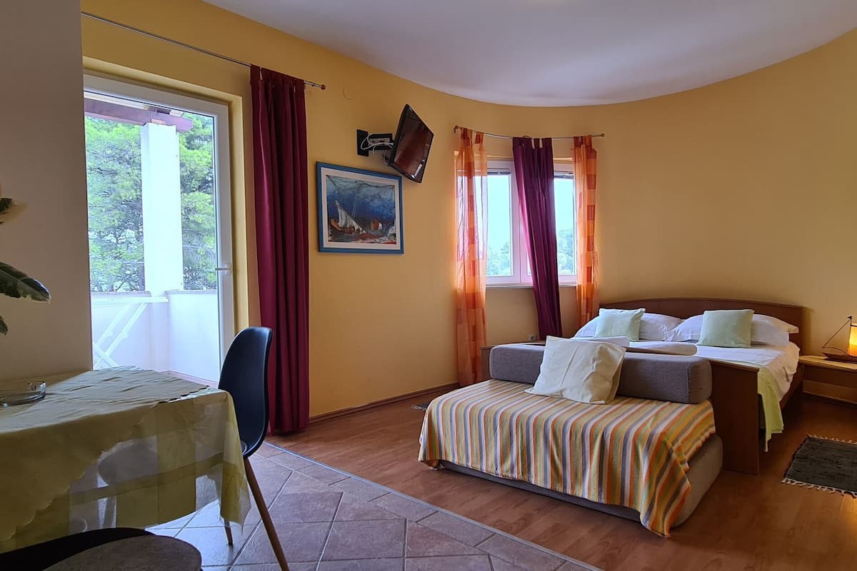 Un cuarto acogedor con una cama, una mesa y una silla. Hay una ventana con cortinas, un cuadro en la pared y una planta sobre la mesa.