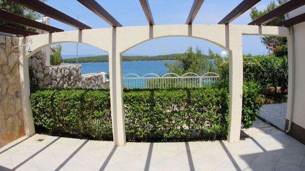 A covered outdoor area with a stone wall, a view of a lake, and a metal fence. - Apartment Nikola (Jelsa)