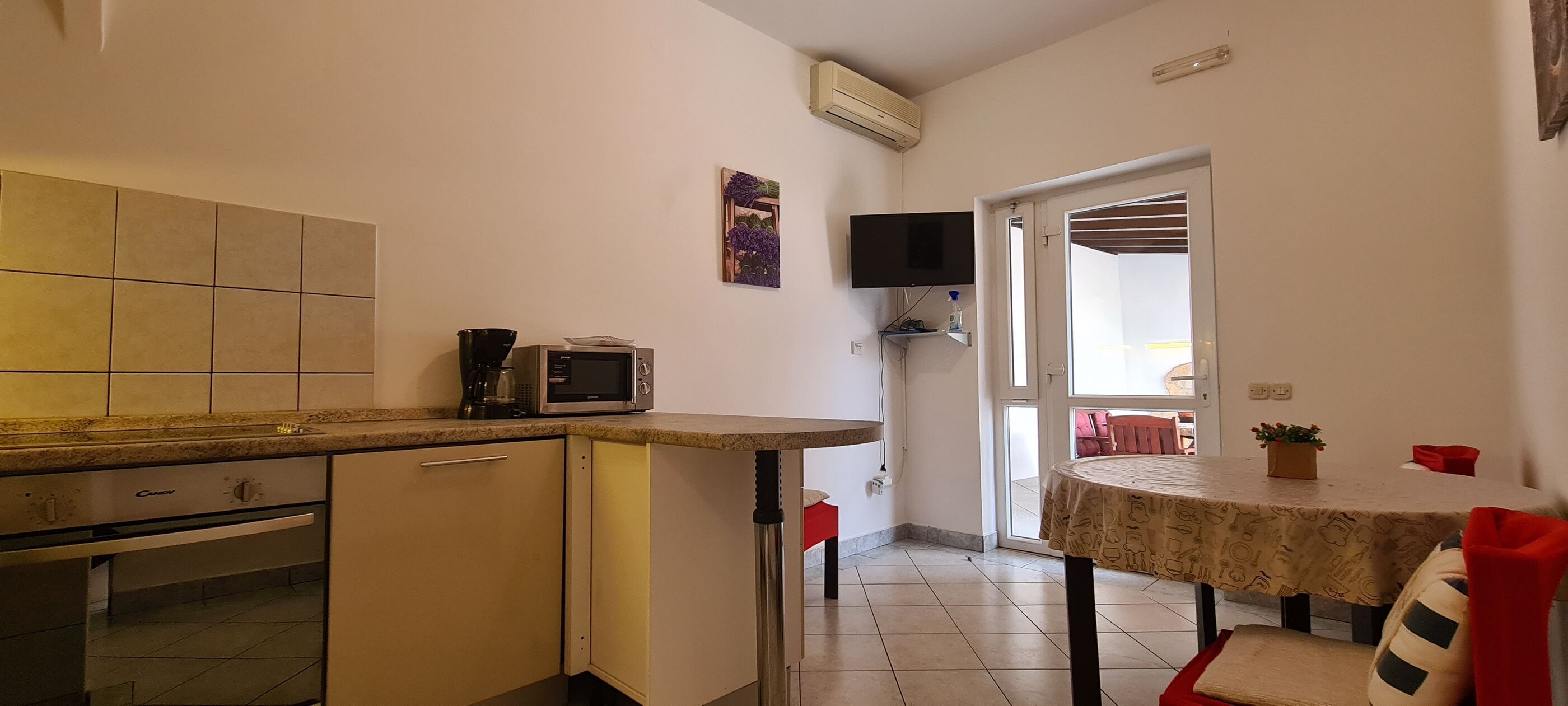Cocina compacta con microondas, cafetera y un pequeño comedor con mesa y sillas.