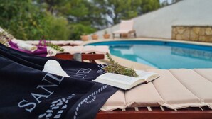 A poolside area with lounge chairs, a book, and a blanket with text. - Apartment Nikola (Jelsa)