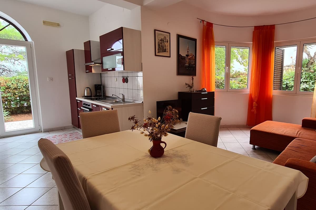 Una sala de estar con sofá, una mesa de comedor con un jarrón de flores y una cocina con armarios y microondas.