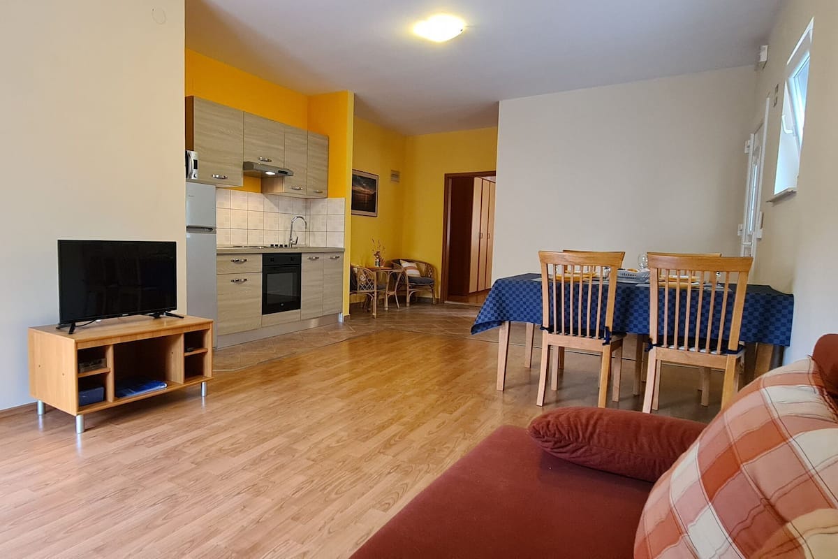 Una sala de estar con un mueble para televisión, un sofá y una zona de comedor con mesa y sillas.