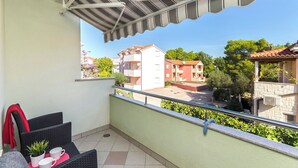 Un balcon avec une rambarde en métal, une petite table sur laquelle est posée une plante en pot, et une serviette rouge accrochée à la chaise.