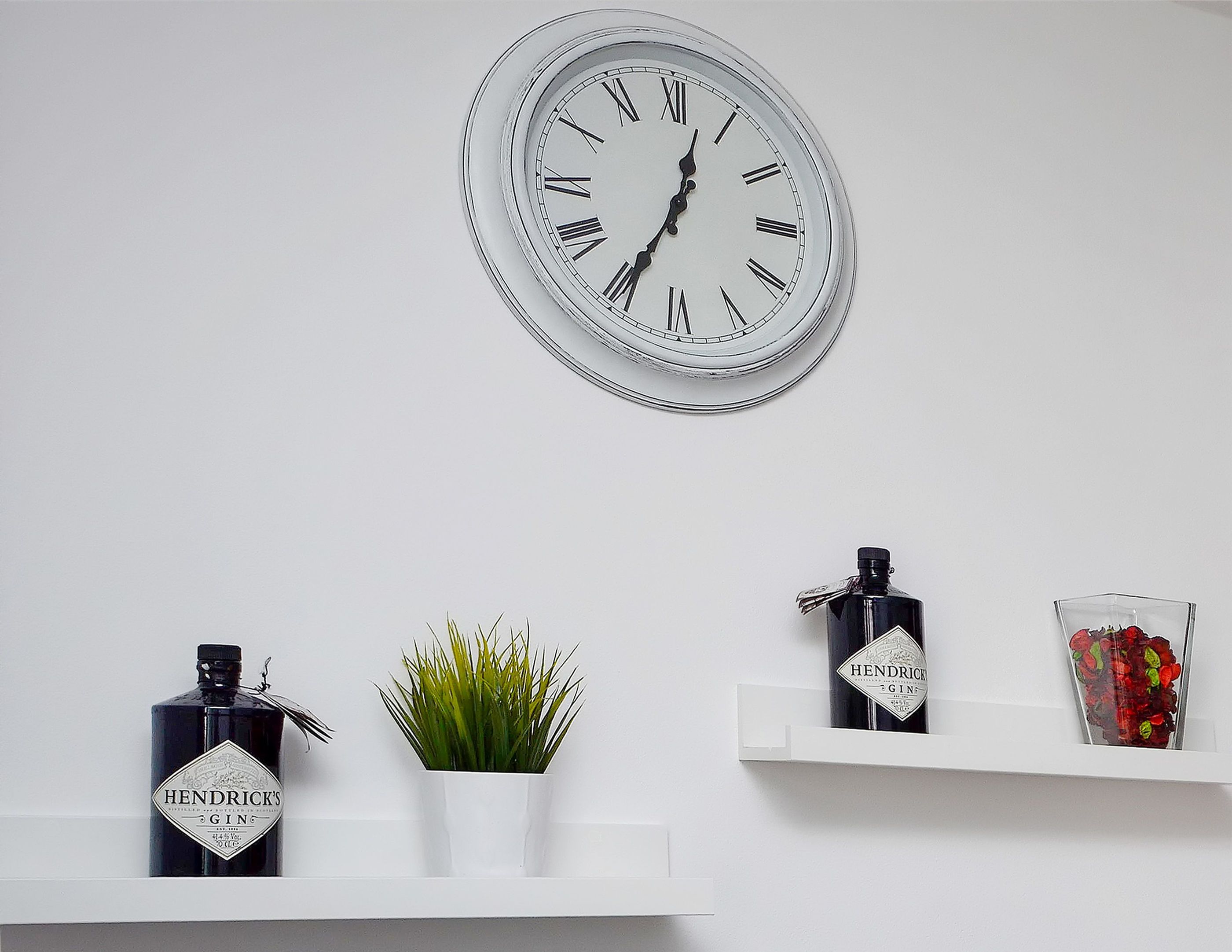 A wall clock, a bottle of Hendrick's gin, a potted plant, and a glass container with red flowers.