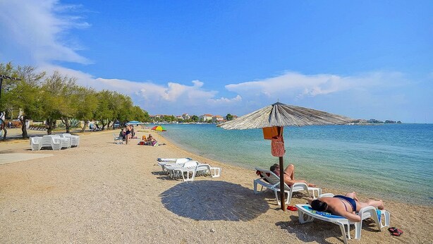 Une plage avec des transats et des parasols, un ciel dégagé et une eau calme.