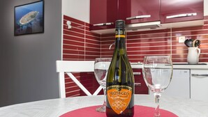 Une bouteille de Prosecco Treviso 2021 est posée sur une table recouverte d’un chemin de table rouge, avec deux verres à vin, et un mur recouvert de carreaux rouges en arrière-plan.