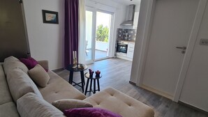 Un salon avec un canapé, une petite table ornée de bougies et une vue sur un balcon et une cuisine.