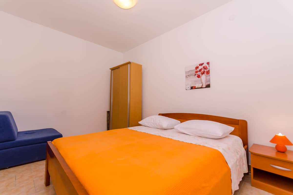 A bedroom with a bed, a nightstand, a blue chair, and a wardrobe.