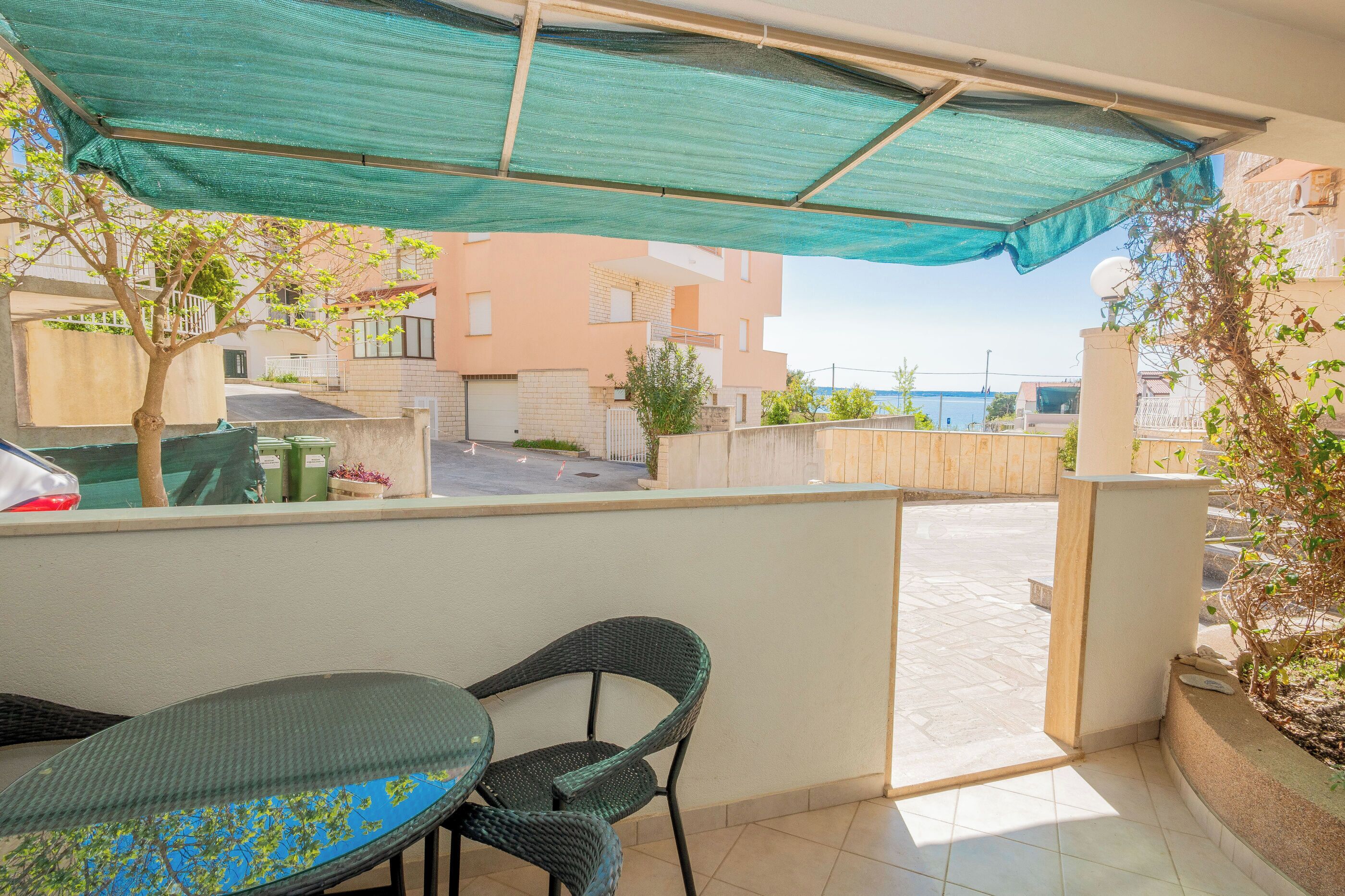 A balcony with a table and chairs, a green canopy, and a view of buildings and the sea.
