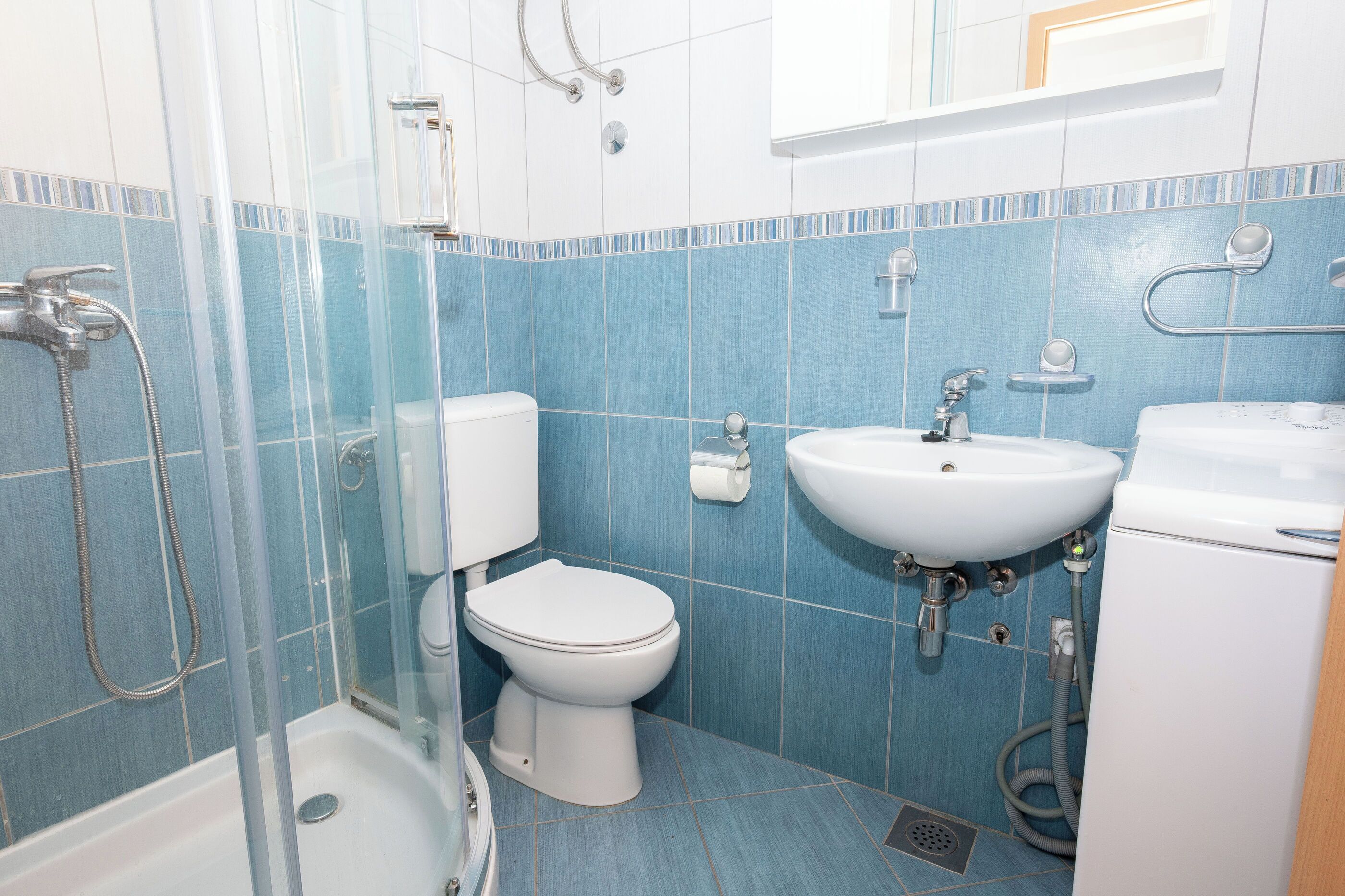 A bathroom with a shower, toilet, sink, and a toilet paper holder.