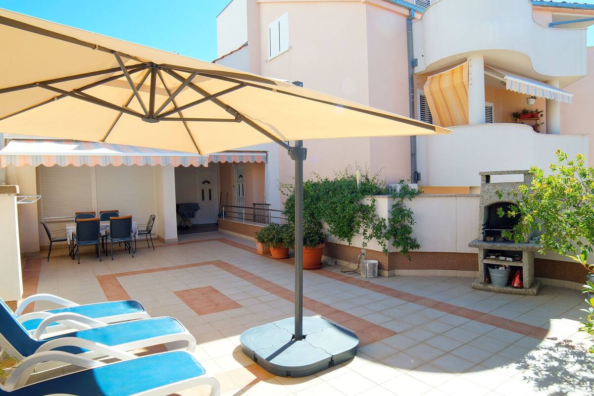 A covered outdoor patio with lounge chairs, a table, and a grill area.