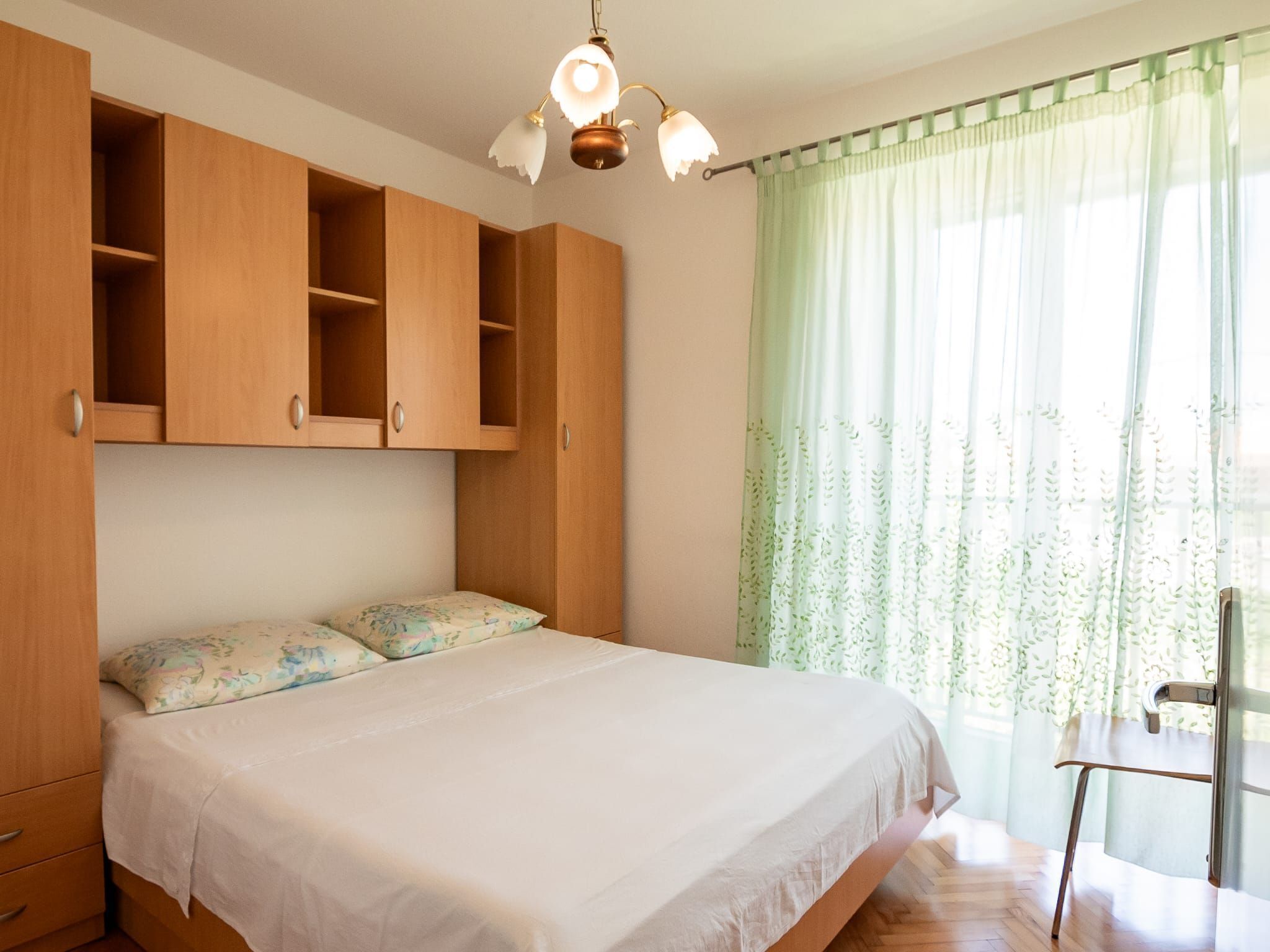 A bedroom with a bed, wooden wardrobe, and a chair.