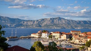 A coastal town with buildings along the waterfront, a dock with boats, and mountains in the background. - Apartments Kaja (Postira)