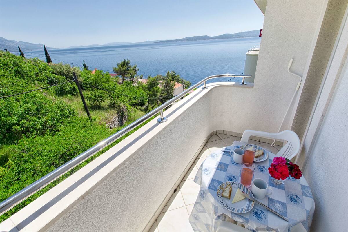 A balcony with a table set for two, overlooking a body of water and greenery.