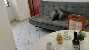 A living room with a grey sofa, a dining table with a bottle of wine, and two paintings on the wall. - Apartments Bogdan (Pisak)